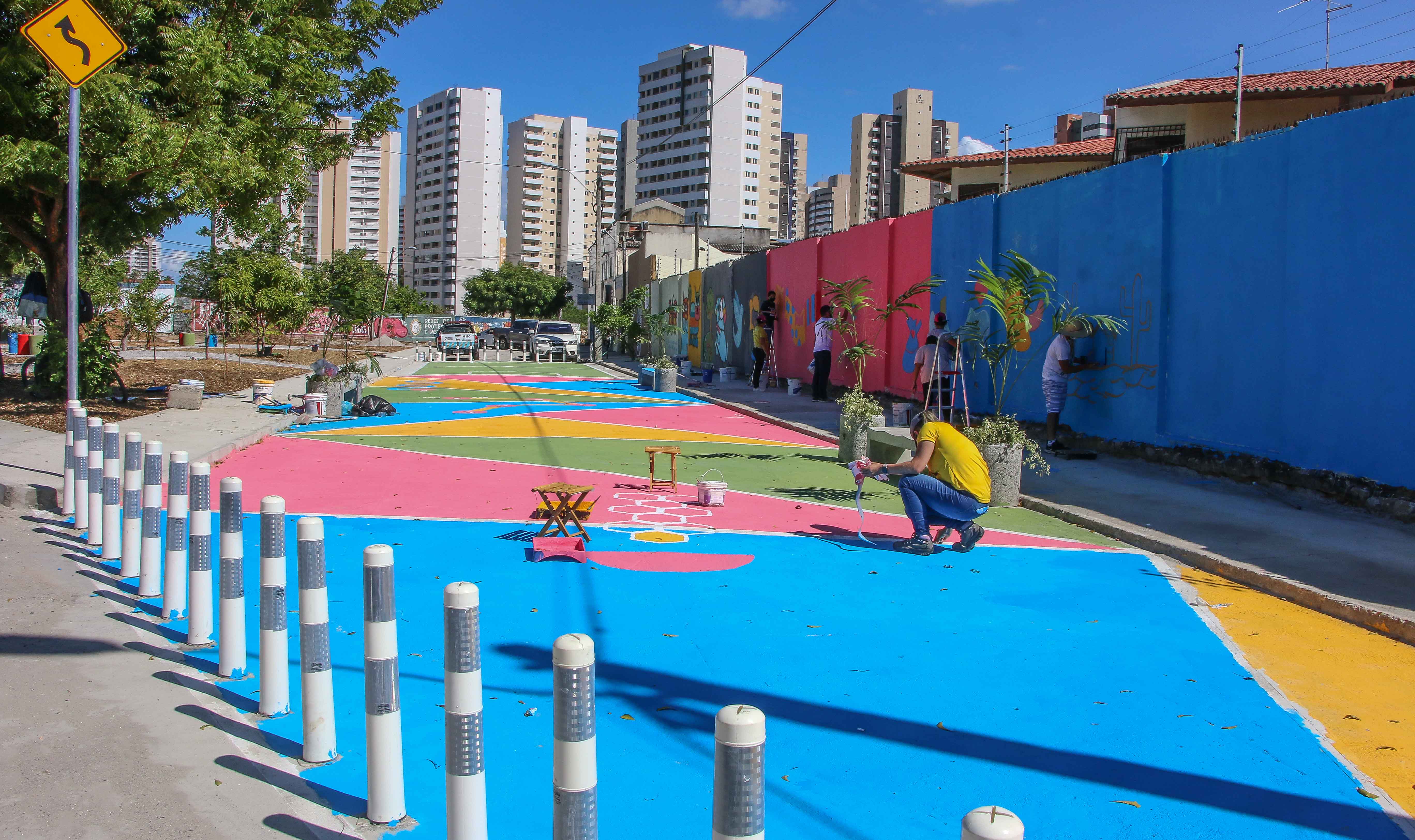 grupo de pessoas pinta uma rua com cores básicas: amarelo, azul e vermelho